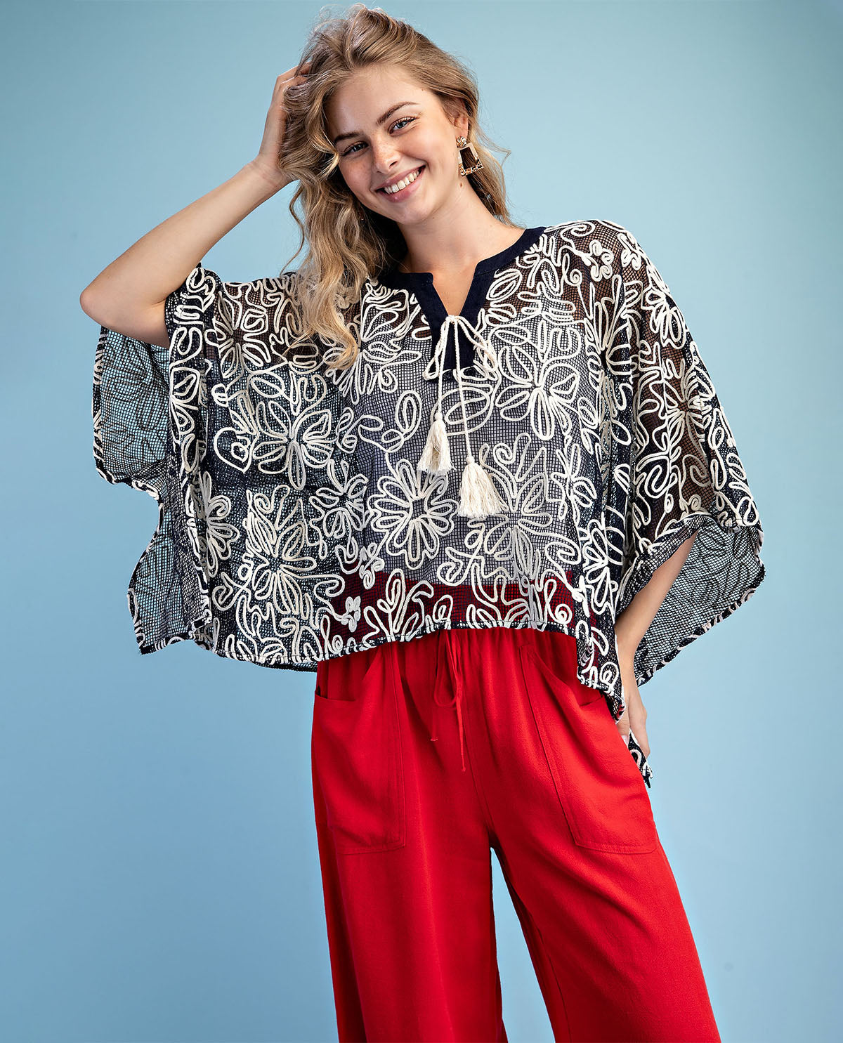 Woman wearing a patterned top and red pants against a blue background