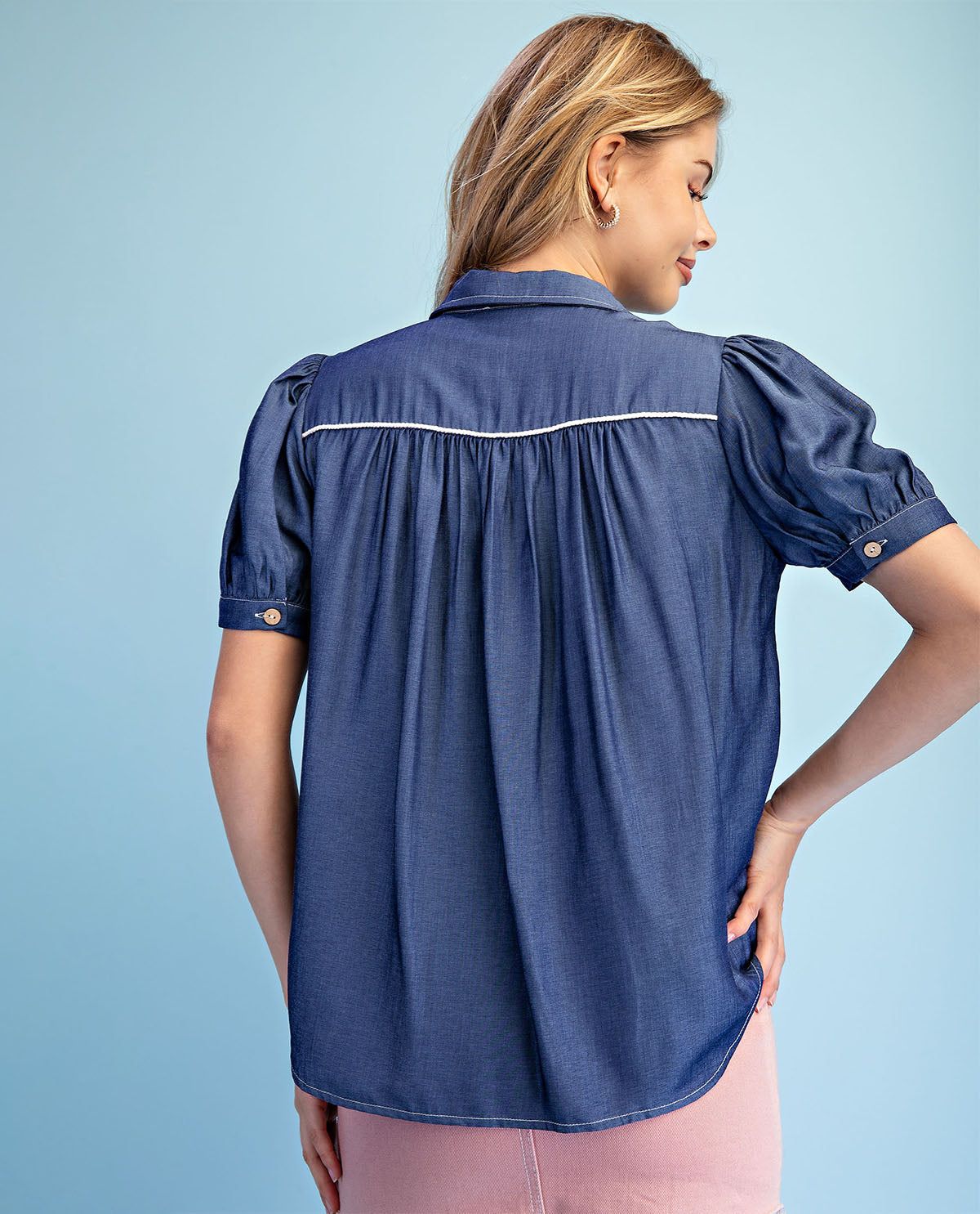 Woman wearing a blue shirt with puff sleeves against a light blue background