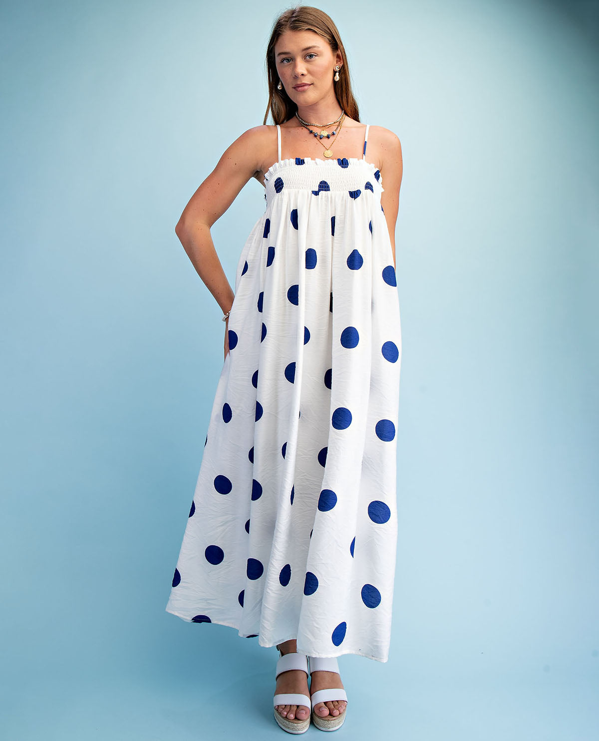 Woman wearing a white dress with blue polka dots against a light blue background