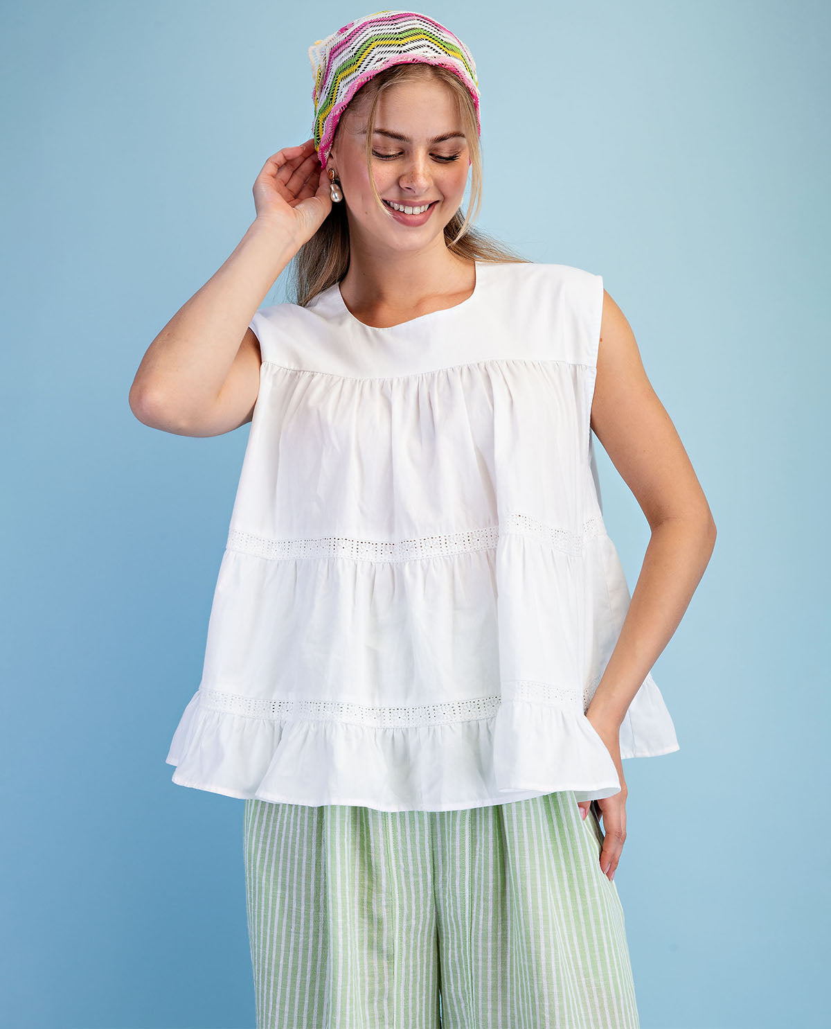 Woman wearing a white sleeveless top and green striped pants against a blue background