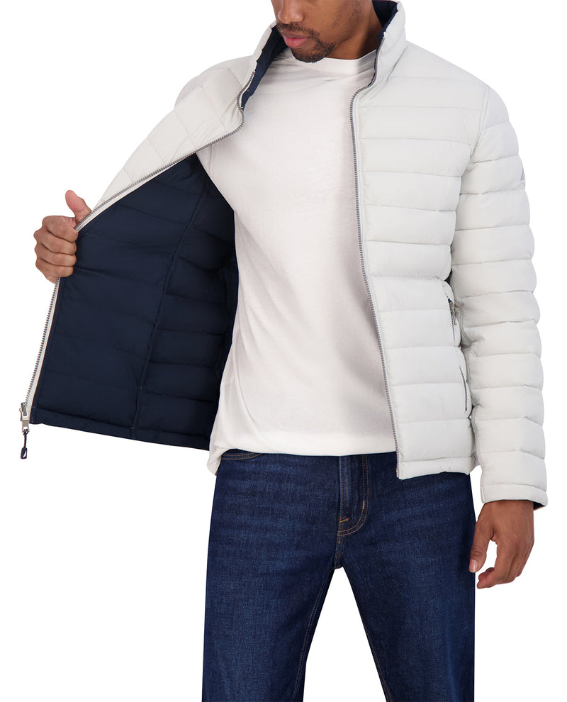 A man wearing a light gray puffer jacket over a white turtleneck sweater and blue jeans, holding the jacket open to show the dark navy lining.