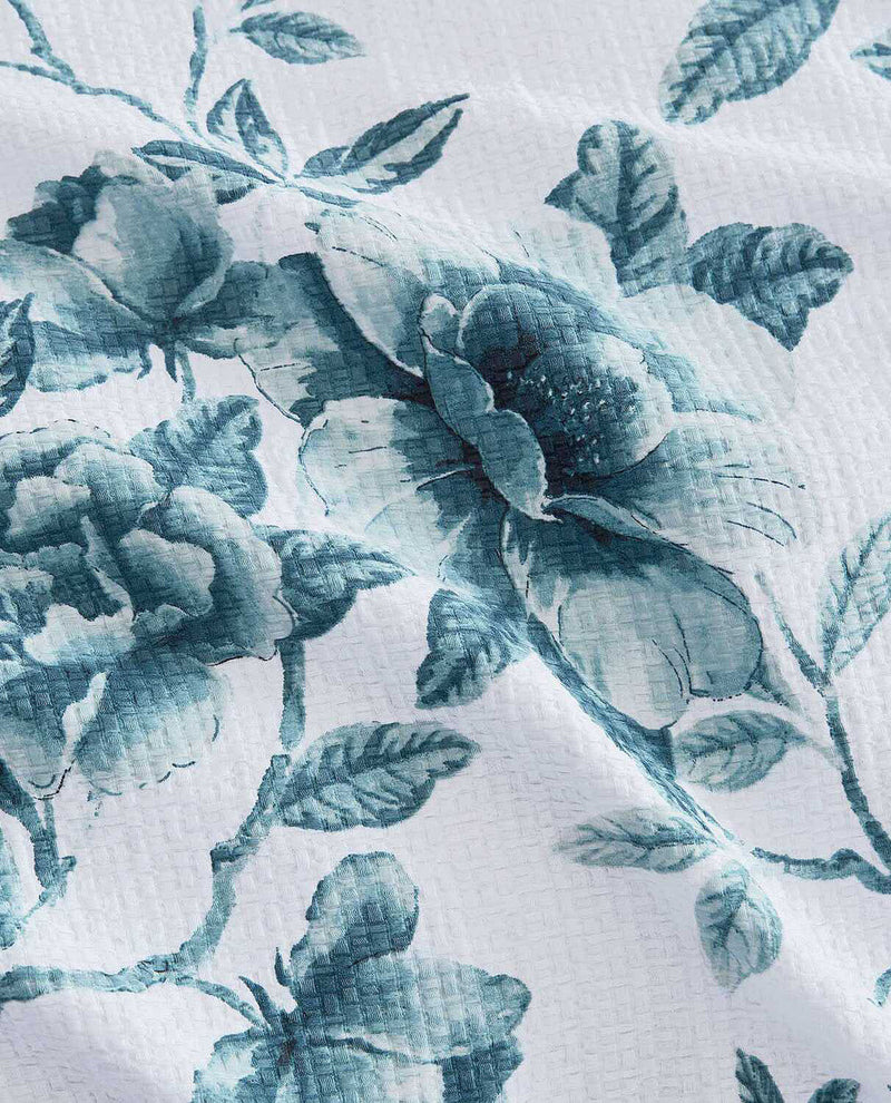 A close-up of a white fabric with a blue-gray floral print, showing the texture of the material and the detailed pattern of roses and leaves.
