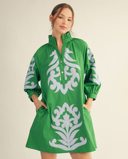 Green dress with white floral patterns worn by a model on a beige background