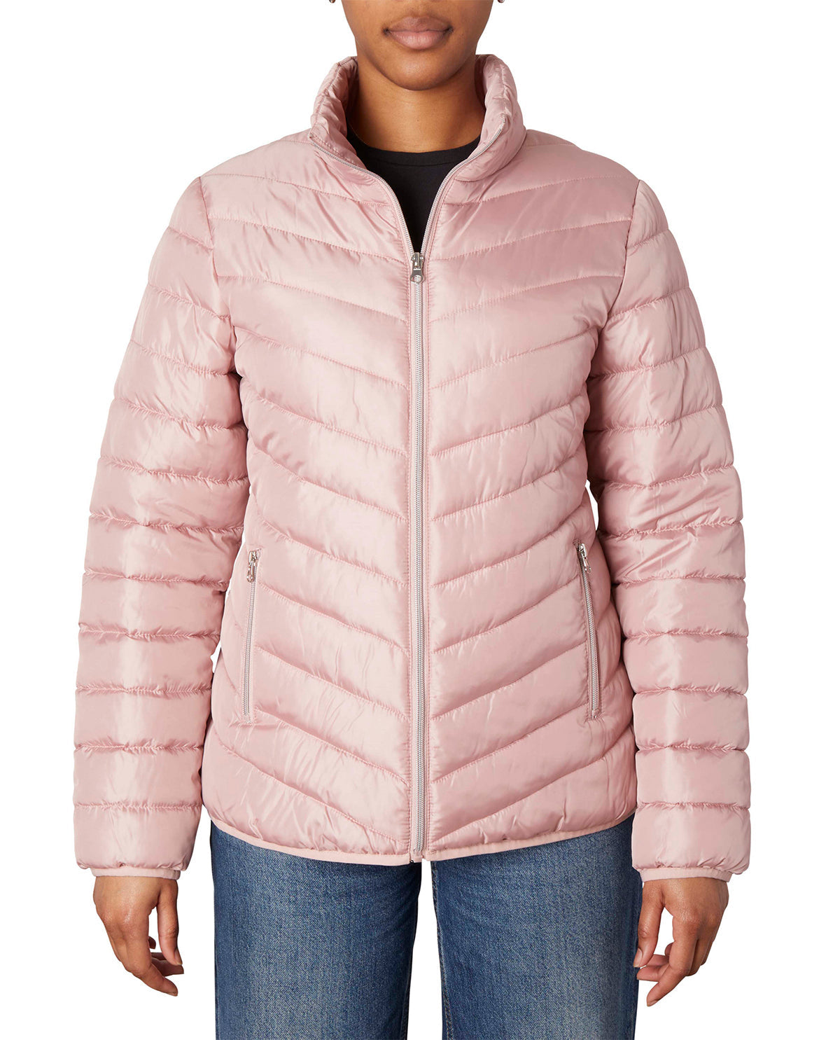A woman wearing a light pink puffer jacket with a stand-up collar and diagonal quilting, paired with blue jeans, shown against a plain white background.